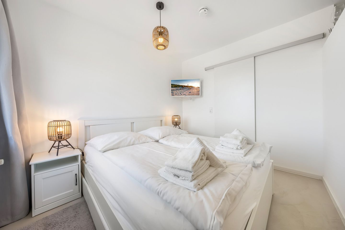 A bedroom with a bed, bedside lamps, a TV, and a wall-mounted picture.