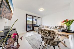 En moderne stue med sofa, spisebord og udsigt gennem en glasdør til et udendørs område.