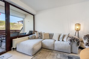 Un salon moderne avec un canapé d’angle, une lampe sur pied et une grande fenêtre.