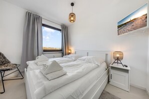 Et moderne soveværelse med en stor seng, et sengebord, en stol, et vindue med udsigt og et TV ophængt på væggen.