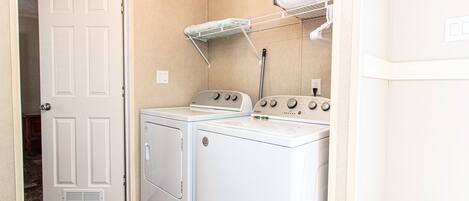 Une buanderie équipée d’un lave-linge et d’un sèche-linge à chargement frontal, d’un étendoir et d’une porte donnant sur une autre pièce.