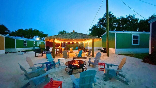 A covered outdoor seating area with chairs and a fire pit, surrounded by a sandy patio. - Sum Beaches Paradise Cottage 1 (Navarre)