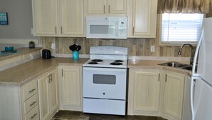 A kitchen with light-colored cabinets, a white stove, a microwave, and a sink. - Sum Beaches Paradise Cottage 1 (Navarre)