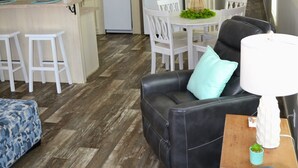 A modern kitchen with white appliances, a dining area with a white table and chairs, and a living area with a black leather sofa and a small table with a lamp. - Sum Beaches Paradise Cottage 1 (Navarre)