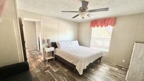 A bedroom with a bed, a nightstand, a ceiling fan, a window with blinds, and a door.