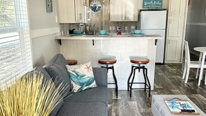 A compact living space with a kitchenette, grey sofa, wooden coffee table, and a small dining area.