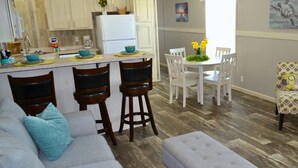 Une cuisine moderne avec des meubles blancs, un réfrigérateur blanc et un coin repas comprenant une table et des chaises blanches.