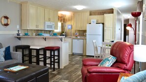 A compact living space with a kitchenette, a dining area, and a seating area with a red leather sofa and a black ottoman.