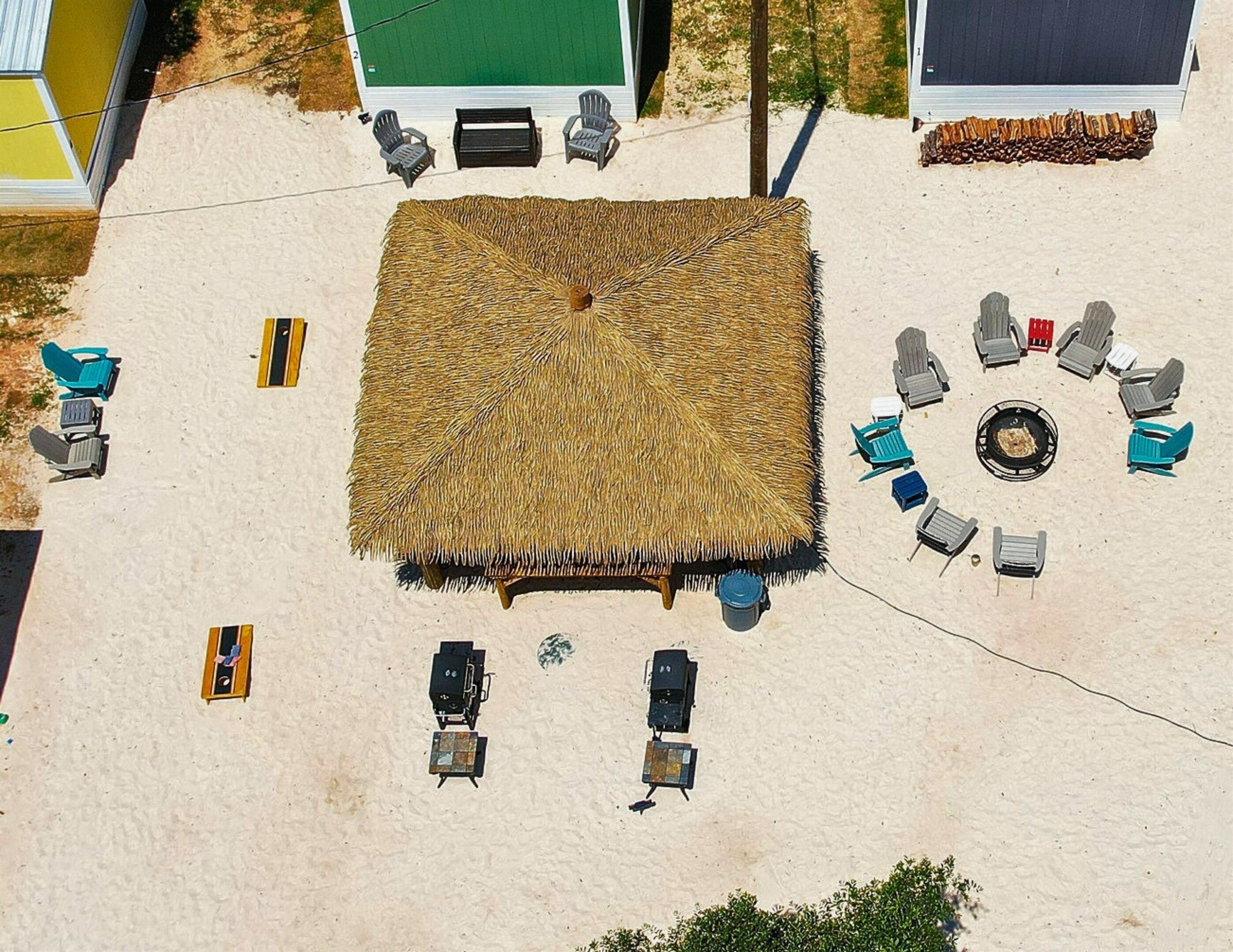 An aerial view of a beach area with a thatched umbrella, multiple lounge chairs, and a barbecue setup.