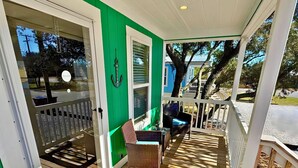 A wooden deck with wicker furniture, a welcome mat, and a green door. - Sum Beaches Paradise Cottage 6 (Navarre)