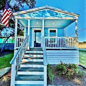 A small, single-story building with a porch, a staircase, and a flag. - Sum Beaches Paradise Cottage 7 (Navarre)
