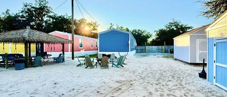 A beach area with a thatched umbrella, a table with chairs, and a blue building.