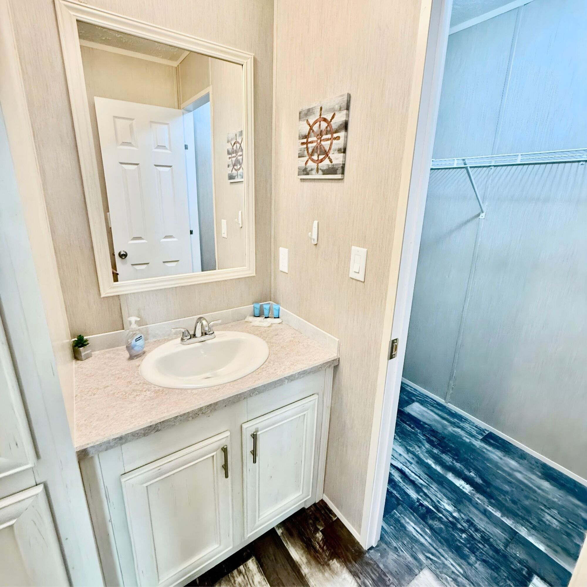 A bathroom with a sink, mirror, and two cabinets. There is a door visible in the mirror reflection.