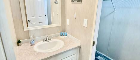 A bathroom with a sink, mirror, and two cabinets. There is a door visible in the mirror reflection.