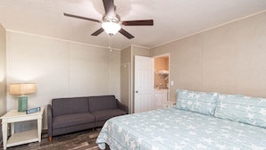 A bedroom with a bed, a gray sofa, a nightstand with a lamp, and a ceiling fan. - Sum Beaches Paradise Cottage 9 (Navarre)