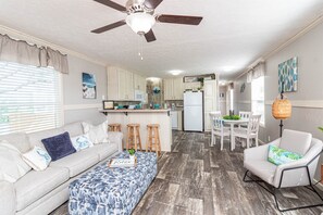 A modern kitchen with white cabinets, a white refrigerator, and a dining area with white chairs and a table.