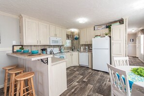 A kitchen with wooden cabinets, a microwave, a refrigerator, and a dining area with a table and chairs.
