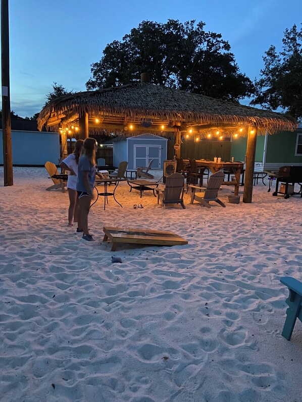 A beachside hut with a thatched roof, surrounded by beach chairs and a dining table.