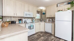 A kitchen with wooden cabinets, a white refrigerator, a microwave, a stove, and a sink. - Sum Beaches Paradise Cottage 9 (Navarre)