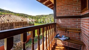 A balcony with a wooden railing, a brick wall, and a view of a hilly landscape. - Apto La Espina 1 - rural apartment in Celada (Villaviciosa) | 4 guests (Celada)