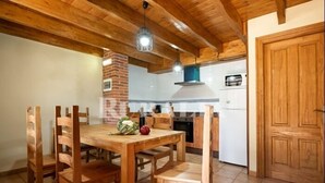 A wooden dining table with chairs, a brick fireplace, and a kitchen area with a white refrigerator and stove. - Apto La Espina 1 - rural apartment in Celada (Villaviciosa) | 4 guests (Celada)