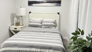 Une chambre à coucher bien rangée, avec un lit, une table de chevet dotée d’une lampe, un objet décoratif et un tableau accroché au mur.