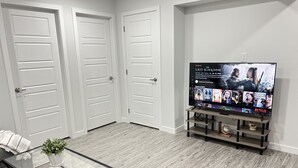 Un salon moderne avec un téléviseur à écran plat diffusant la série « The Last Kingdom ». On y trouve trois portes blanches, une table basse en verre avec des livres et un plancher en bois.