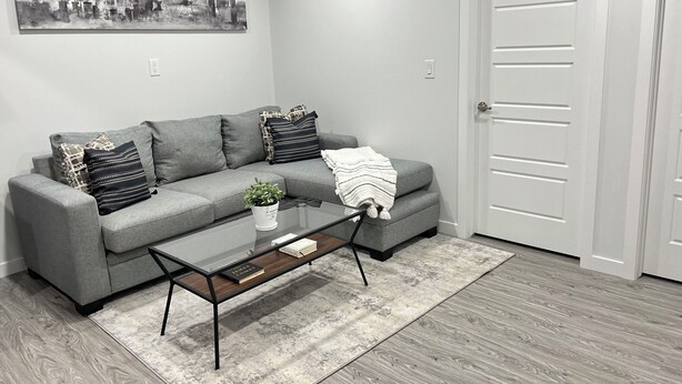 Un salon moderne avec un canapé gris, une table basse en verre et un tableau représentant un paysage urbain accroché au mur.