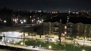 A nighttime view of a riverside area with buildings, streetlights, and a bridge.