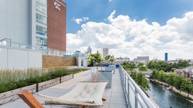 A rooftop terrace with two hammocks, a river view, and a modern building with a red brick section.