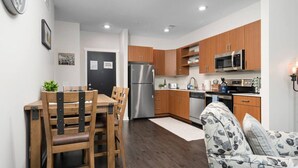 Una cocina moderna con armarios de madera, electrodomésticos de acero inoxidable, un comedor con mesa y sillas, y un sofá estampado.