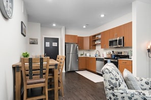 A modern kitchen with wooden cabinets, stainless steel appliances, and a dining area with a table and chairs.