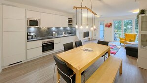 Une cuisine moderne avec des meubles blancs, une table à manger en bois et un luminaire suspendu.