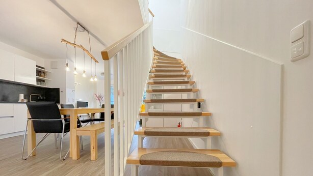 Un intérieur moderne avec un escalier en bois, un coin repas et une cuisine.