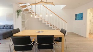 Un salon moderne avec une table à manger en bois, des chaises noires, un escalier avec des rampes blanches et un luminaire suspendu.