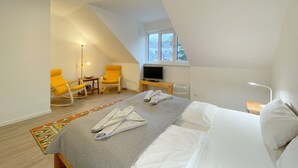 Une chambre à coucher avec un lit, deux chaises jaunes, une télévision et une fenêtre.