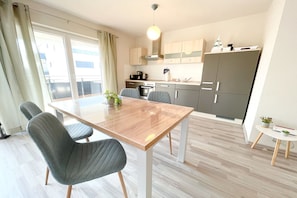 A modern kitchen with a dining table and chairs, a small island, and a view of the city. - Relaxed vacation in the Strandstraße: Your dream home by the sea! - (Loddin)