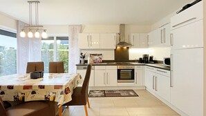 Une cuisine moderne avec des meubles blancs, une table à manger avec des chaises et une grande fenêtre qui laisse entrer la lumière naturelle.