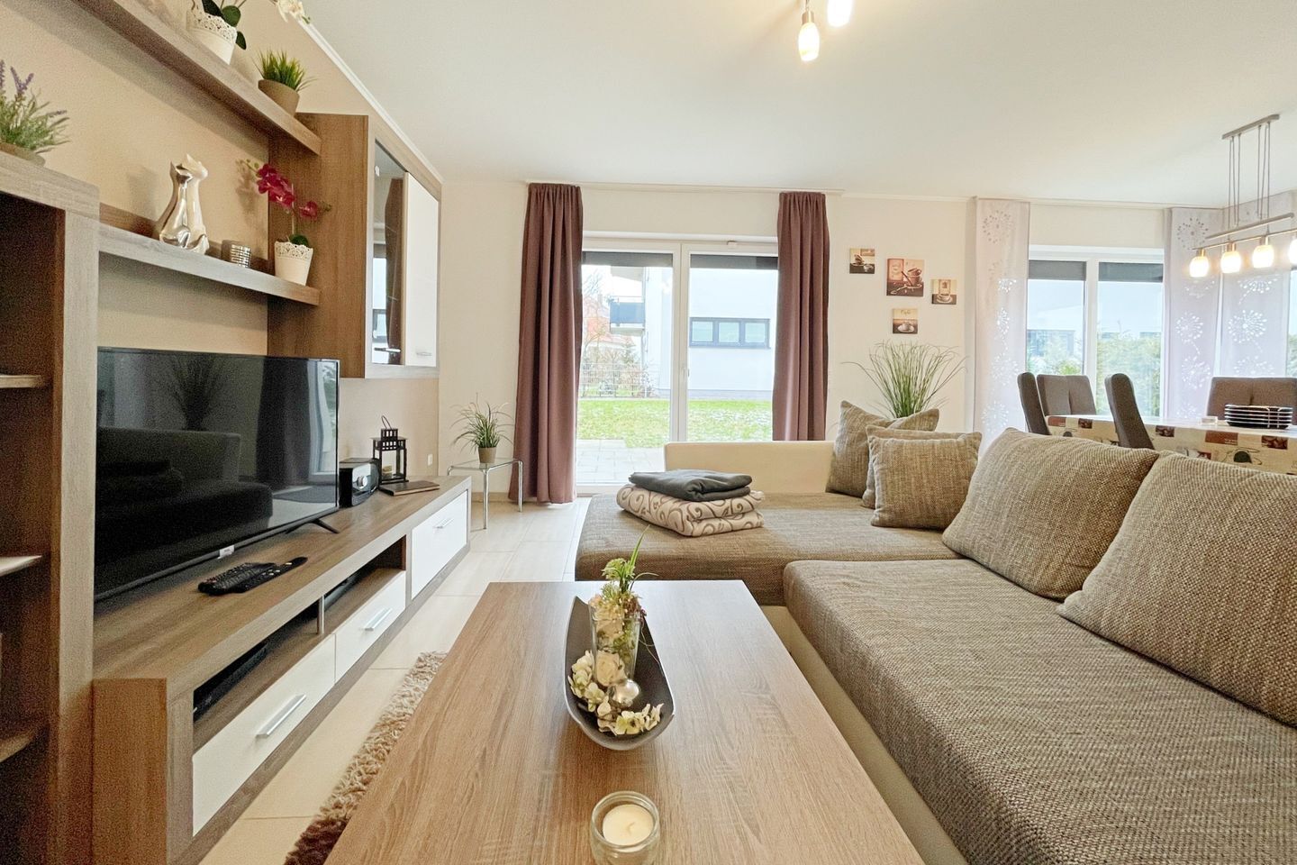 A modern living room with a flat-screen TV, a wooden coffee table, and a beige sofa.