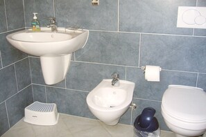 Un bagno con lavabo su piedistallo, bidet, WC e dispenser di sapone a parete.