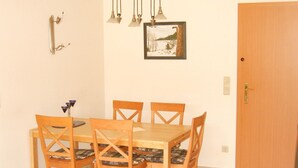 Un coin repas avec une table en bois et quatre chaises, un tableau au mur et une porte sur la droite.