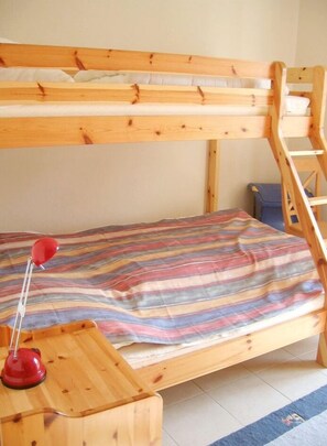 Un letto a castello con struttura in legno, copripiumone a righe e una lampada rossa su un comodino in legno.