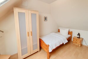 A bedroom with a wooden wardrobe, a single bed, a bedside table, and a small desk. - Relax on 75 square meters in the Hansehuus, for 5 people, on the sunny island of Usedom. - (Zempin)