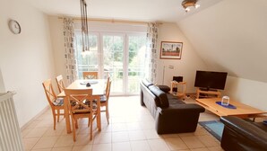 A modern living room with a dining table, chairs, a sofa, a TV, and a radiator. - Relax on 75 square meters in the Hansehuus, for 5 people, on the sunny island of Usedom. - (Zempin)