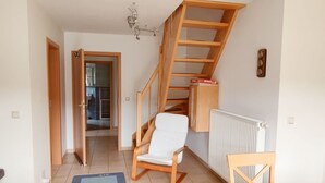 A room with a wooden staircase, a white chair, a radiator, and a door leading to another room. - Relax on 75 square meters in the Hansehuus, for 5 people, on the sunny island of Usedom. - (Zempin)