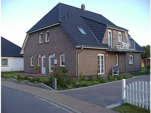 A two-story brick house with a sloped roof, a front porch, and a small garden with flowers and shrubs. - Relax on 75 square meters in the Hansehuus, for 5 people, on the sunny island of Usedom. - (Zempin)