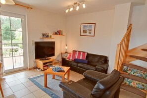 Ein Wohnzimmer mit Fernseher, Sofa, Couchtisch und einer Treppe.