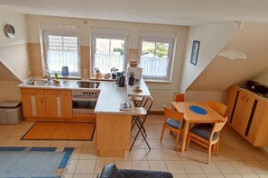 Eine kompakte Küche mit einer zentralen Kochinsel, einem Essbereich mit Tisch und Stühlen sowie einer kleinen Sitzecke mit einer Couch.