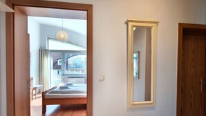 A bedroom with a bed, a window, a hanging light fixture, and a door.