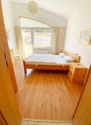 Une chambre à coucher avec un lit en bois, une fenêtre avec des rideaux, une table de chevet et une commode.